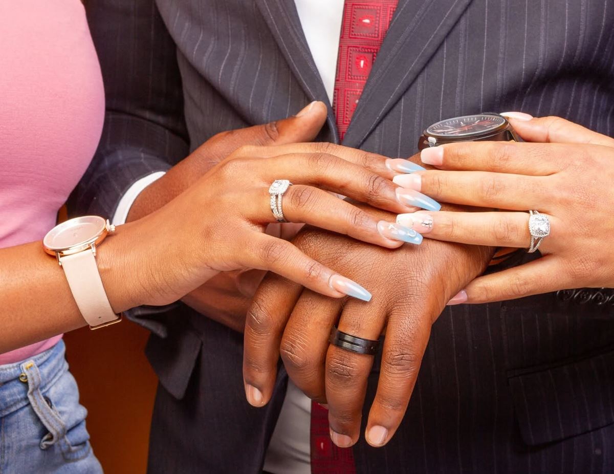 A couple's hands together showing matching rings, her halo ring and his black band