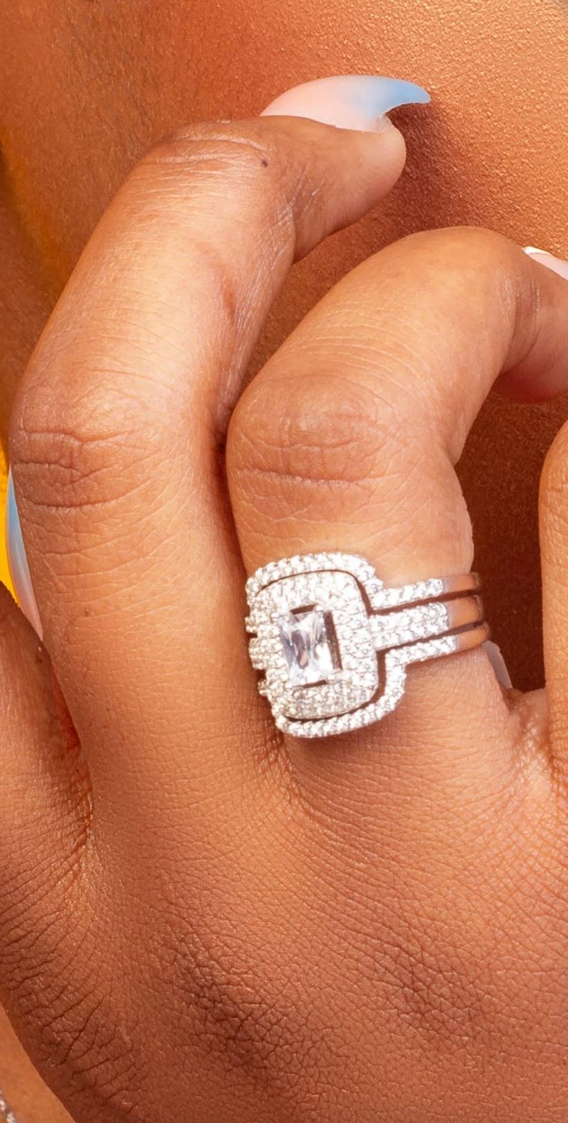 Stacked sterling silver rings with an emerald-cut centre stone and halo, worn on a hand